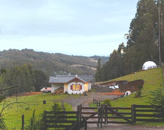 Imagen de una cabaña en el campo con fondo de montaña y bosque